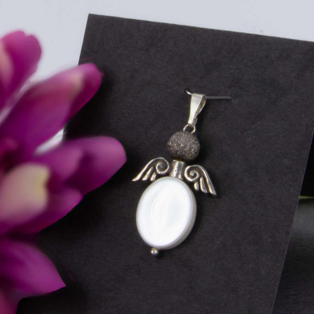 Engel aus Perlmutt mit Silberflügeln und satinierter Perle auf schwarzen Aufsteller mit Blumenblättern